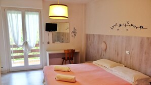 A bedroom with a bed, a desk, a chair, a TV, and a balcony with curtains. - Hotel Dolomiti Levico (Levico Terme)