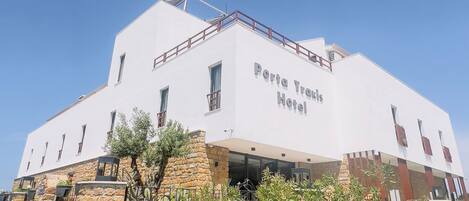A white building with a stone base and a sign reading "Porta Traris Hotel".