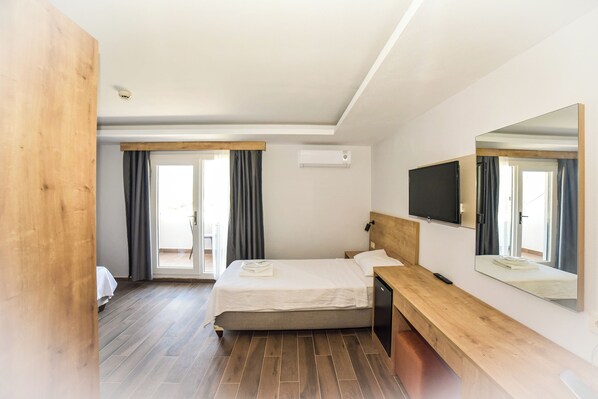 A hotel room with a bed, a wooden bench, a TV, and a large mirror.
