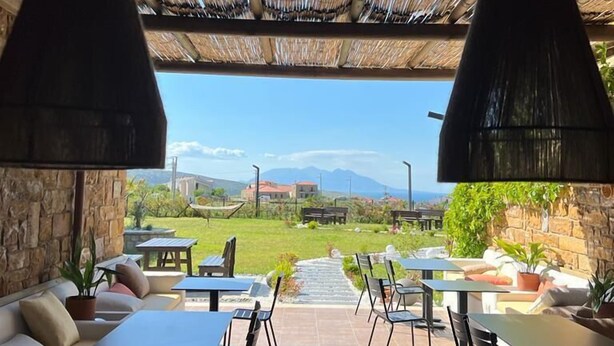Un espacio de comedor al aire libre con paredes de piedra, lámparas colgantes negras y vistas a montañas distantes.