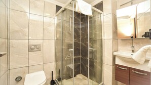 Un baño moderno con ducha de vidrio, inodoro y lavamanos con espejo arriba.