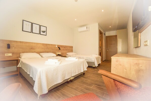 A hotel room with two beds, a wooden headboard, a small table, and a chair. There are framed pictures on the wall and an air conditioning unit on the wall. - Porta Trakis Hotel (Gökçeada)