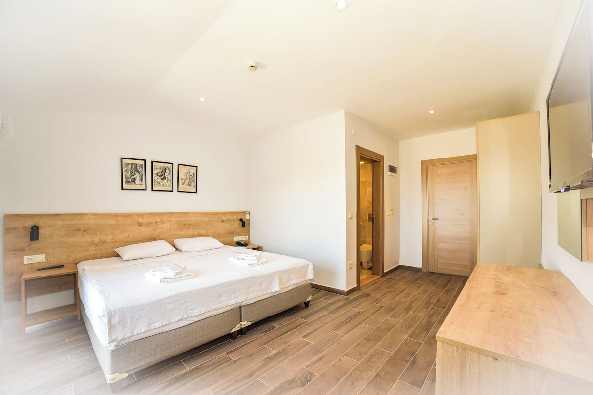 A modern hotel room with a large bed, bedside tables, a wooden headboard, and a small desk.