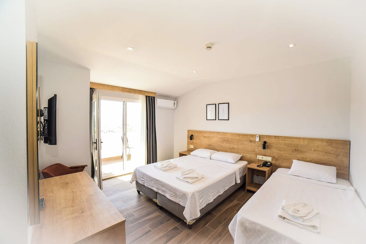 A hotel room with two beds, a wooden headboard, a flat-screen TV, a desk, and a sliding glass door leading to a balcony.