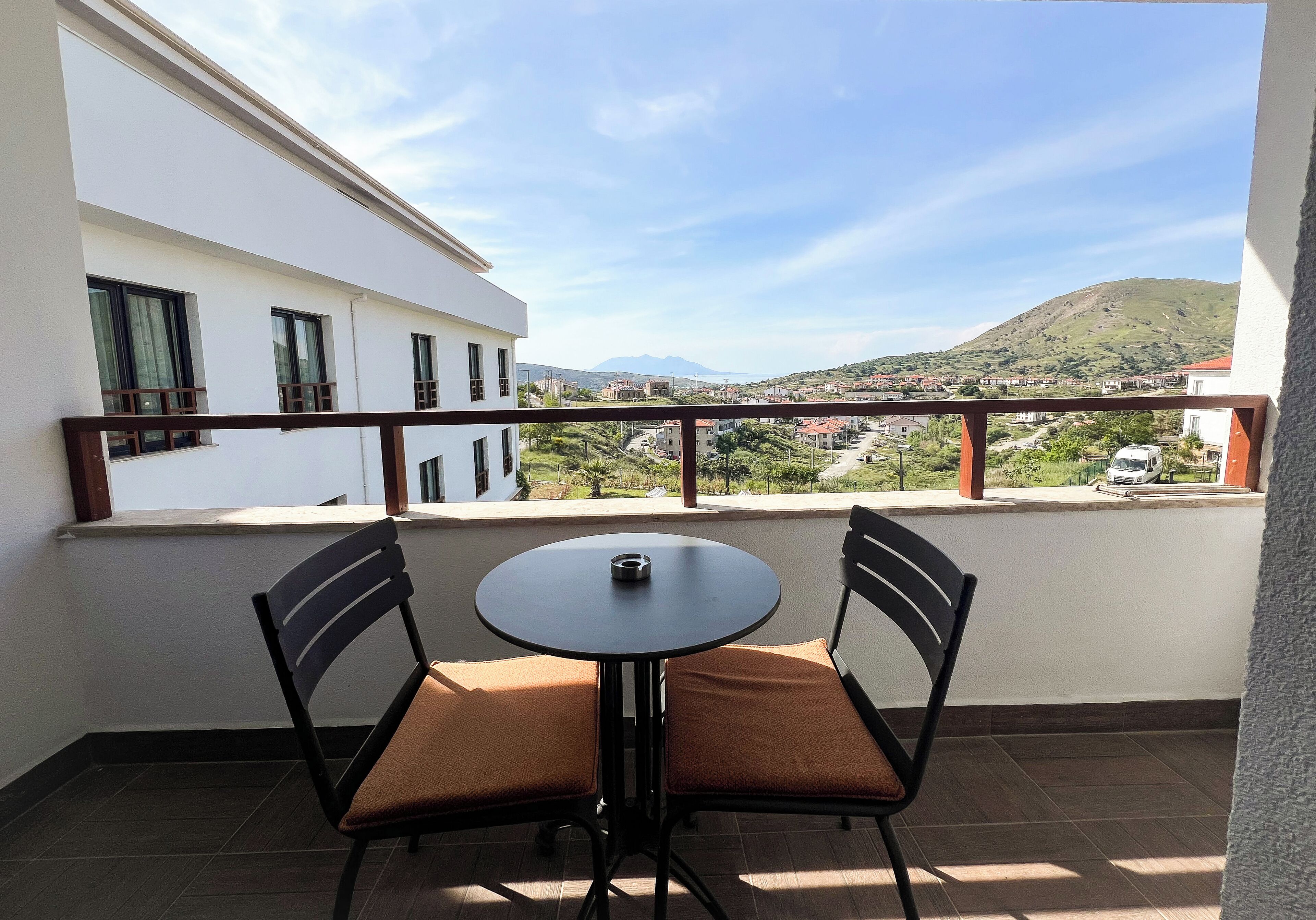 Un balcón con dos sillas y una mesa, con vista a un pueblo y una colina.