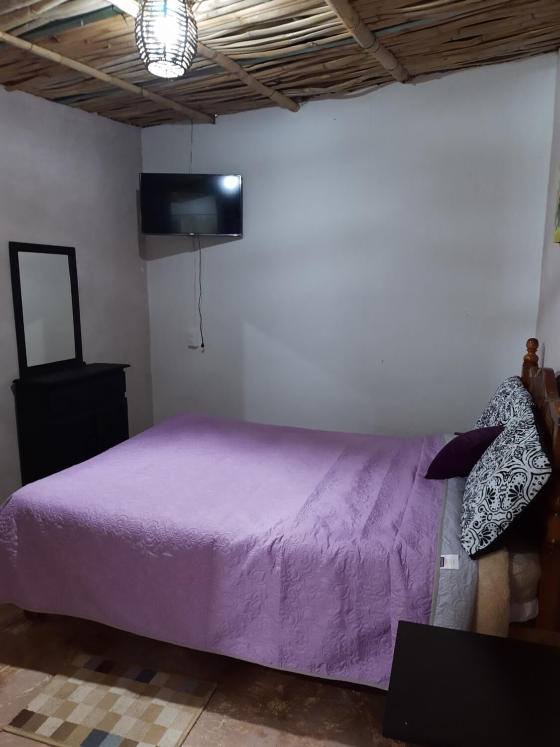 Een slaapkamer met een bed, een aan de muur bevestigde televisie, een houten hoofdbord en een klein dressoir.