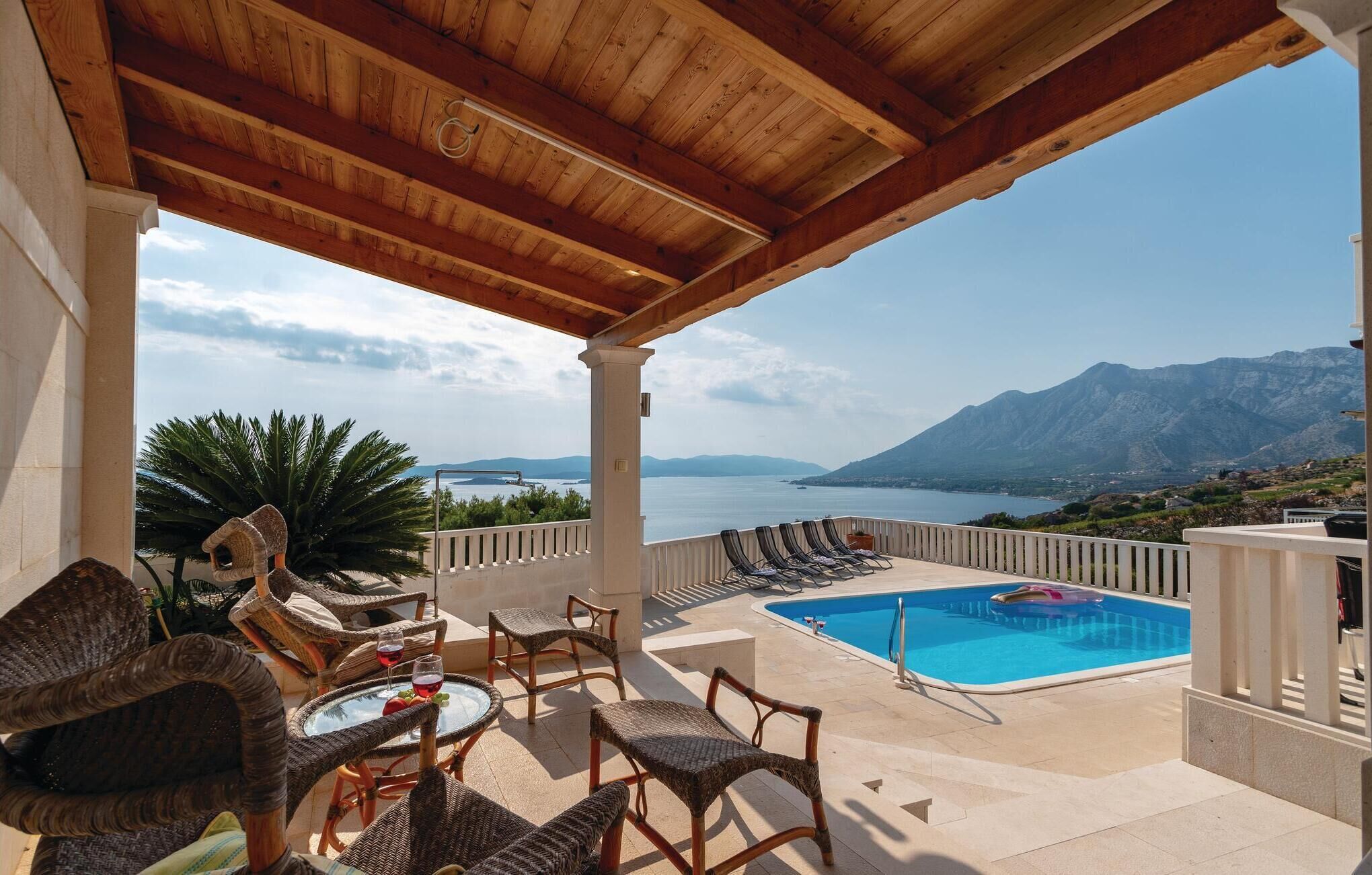 Eine Terrasss mit Korbmöbeln, einem Pool und Blick auf das Meer und die Berge.