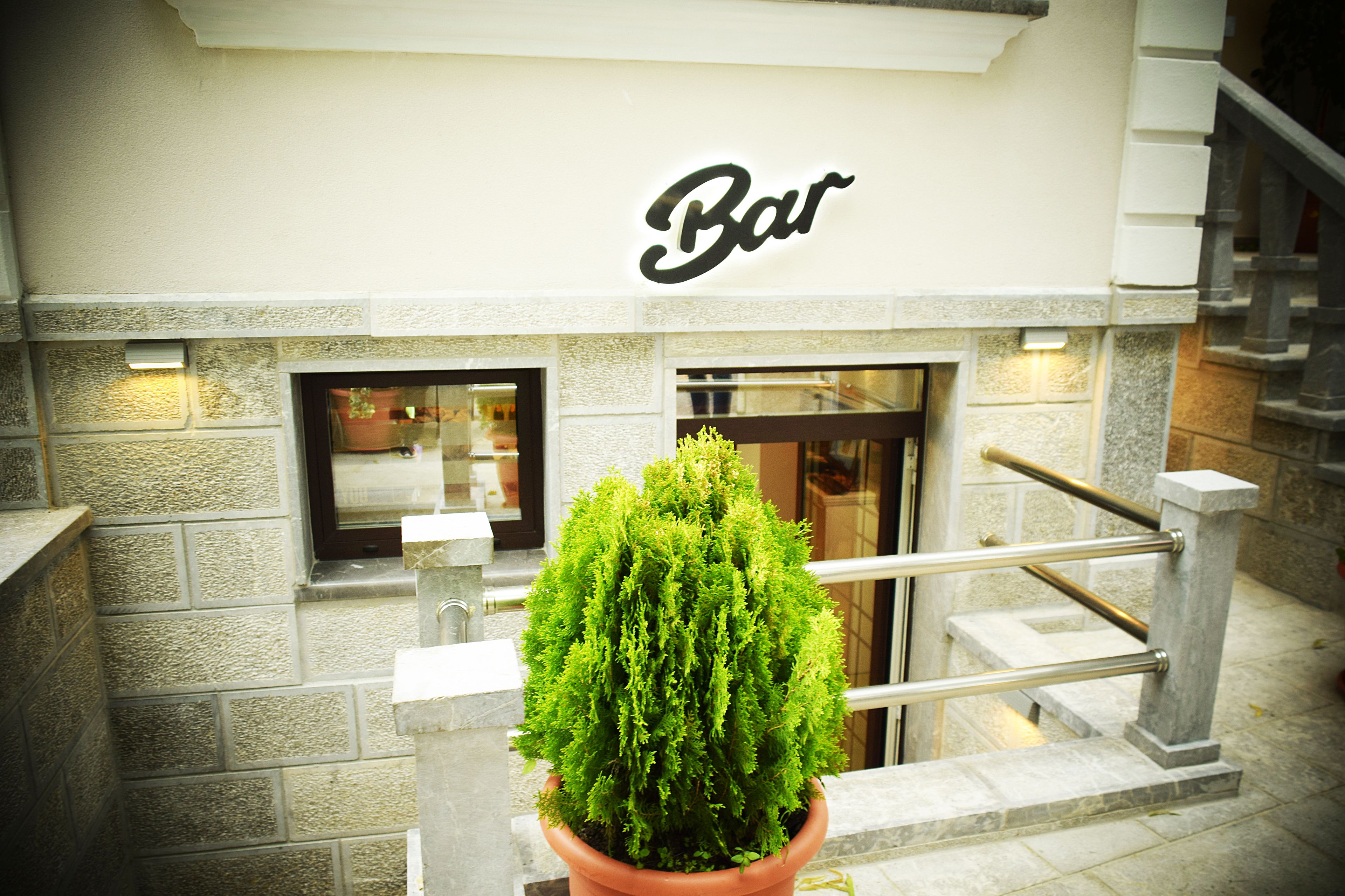 A bar with a sign above the entrance, a potted plant in the foreground, and a staircase to the right.