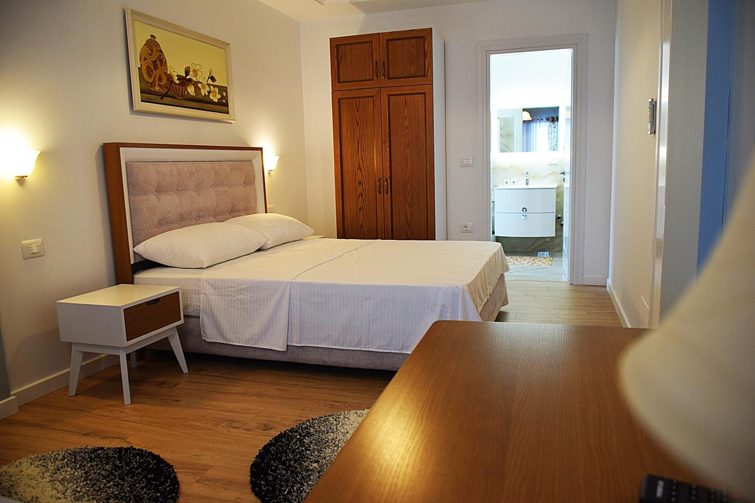A bedroom with a bed, bedside table, wooden wardrobe, and a painting on the wall.