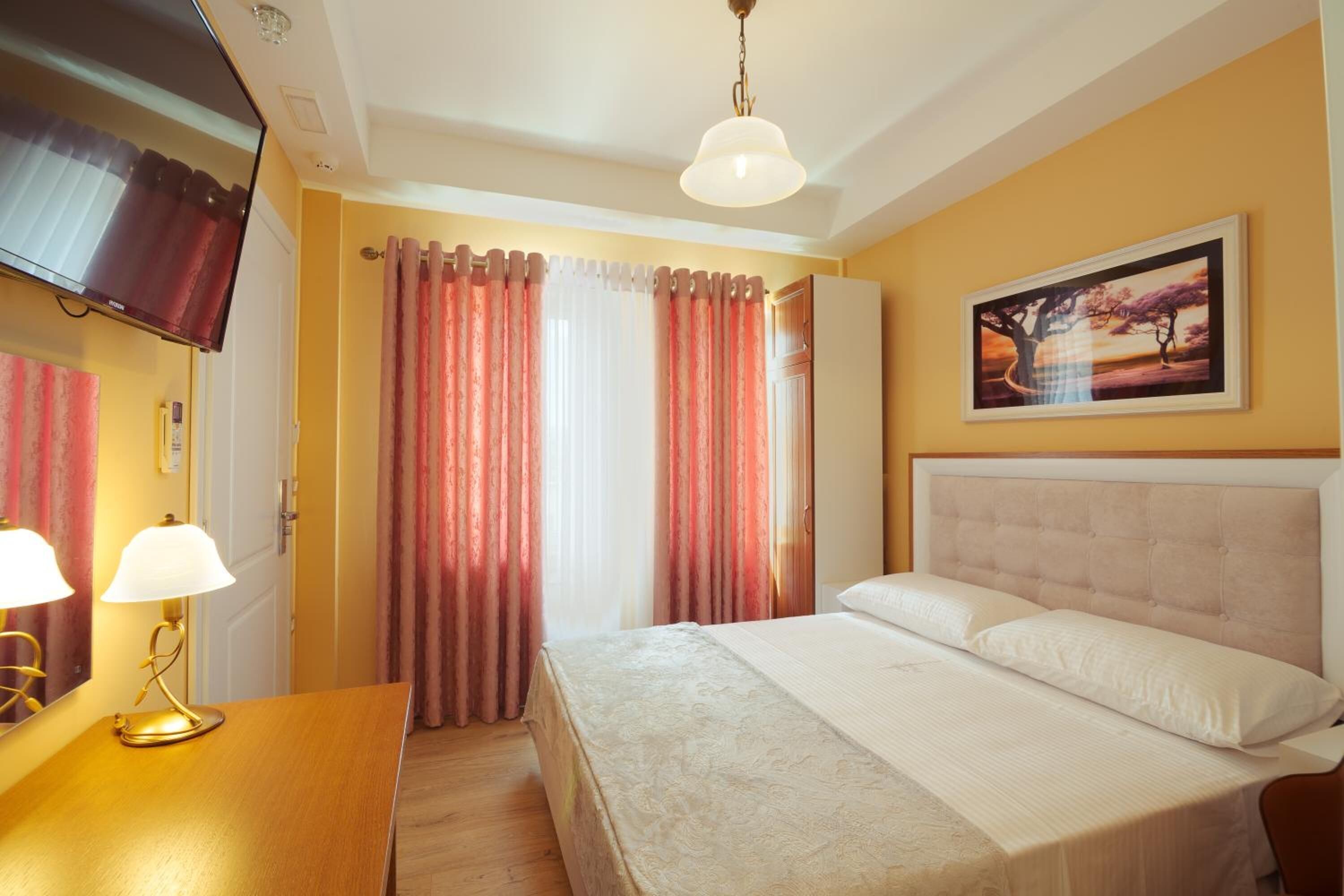 A hotel room with a bed, a desk with lamps, a television, and a painting on the wall.