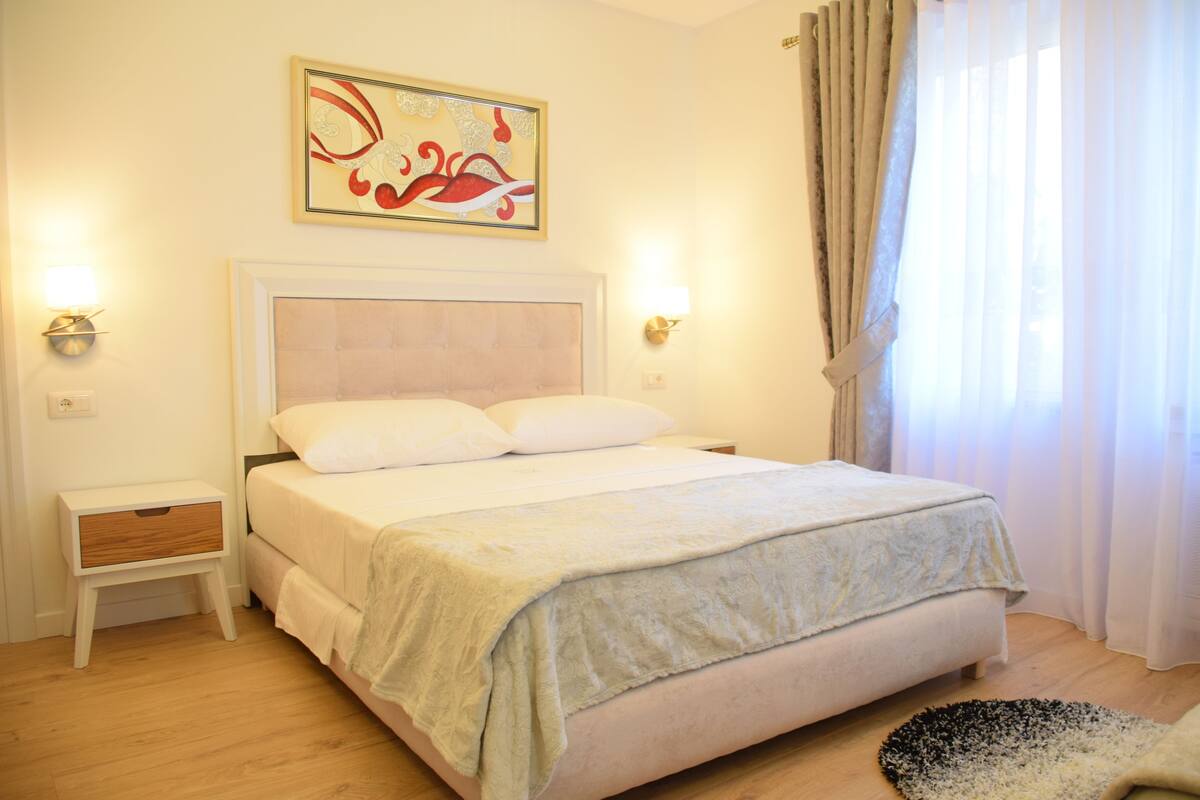 Une chambre à coucher bien rangée, avec un lit, des tables de chevet et un tableau accroché au mur.