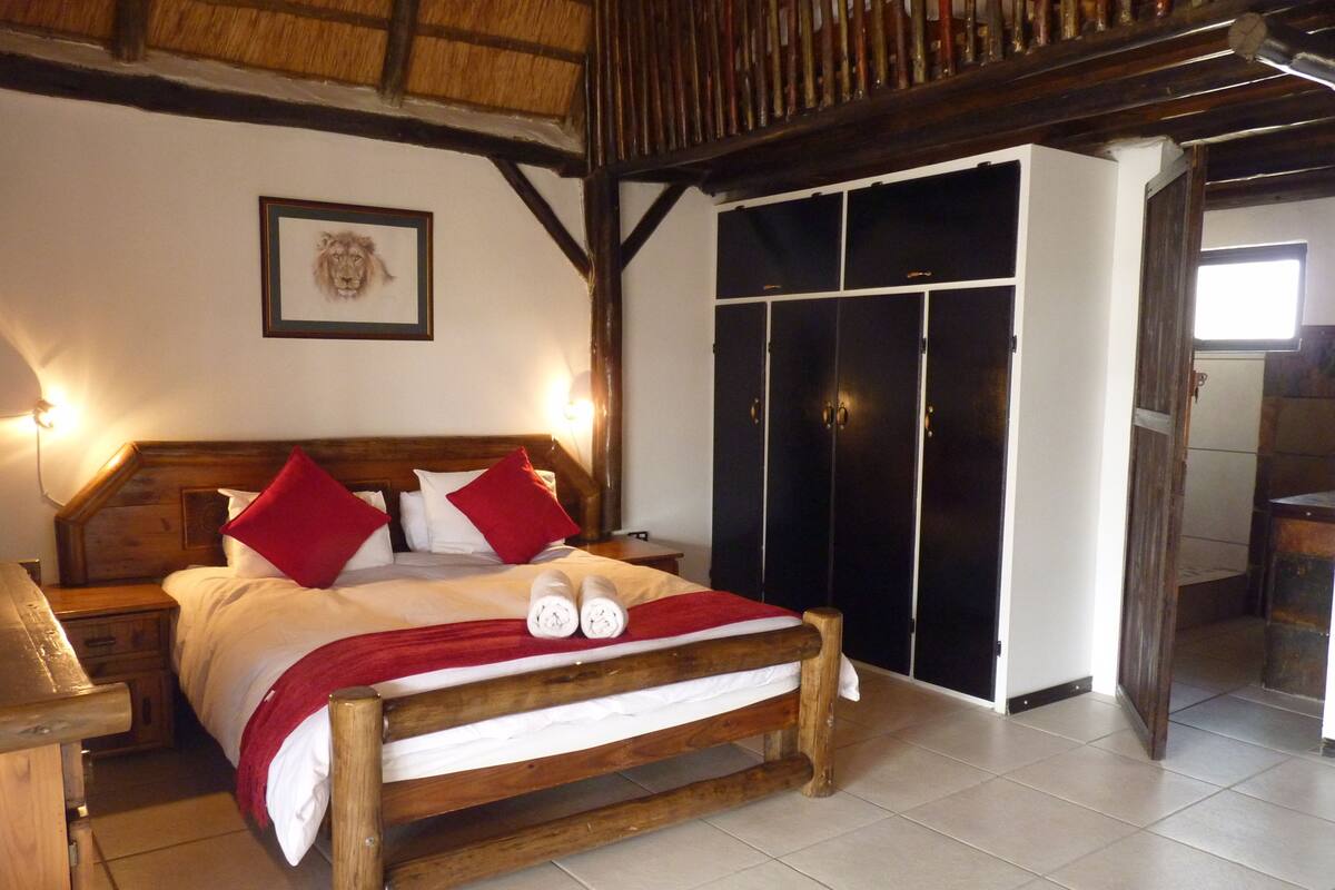 A wooden bed with red pillows and a red throw blanket, a wooden nightstand, a framed picture on the wall, and a black wardrobe with multiple doors.