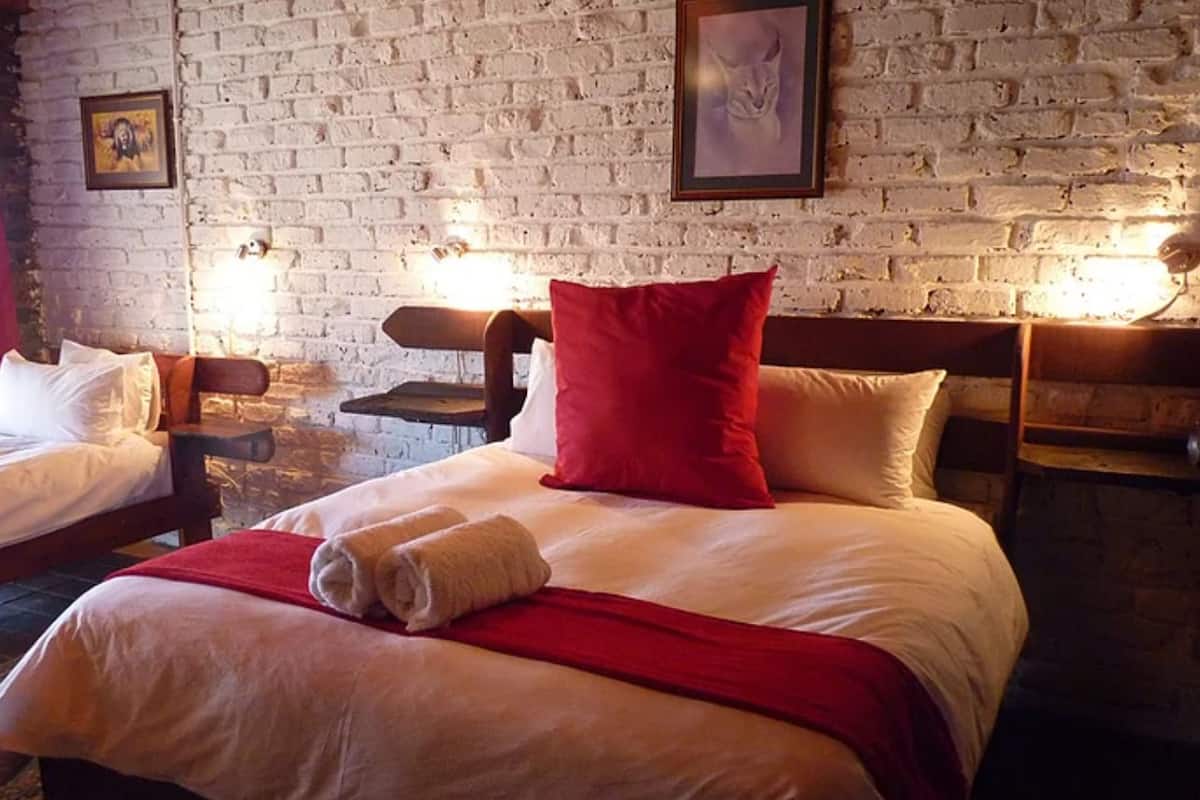 A hotel room with two beds, a brick wall, and framed pictures.