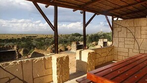 A covered outdoor area with a wooden bench and stone walls, overlooking a landscape with sparse vegetation and distant hills.