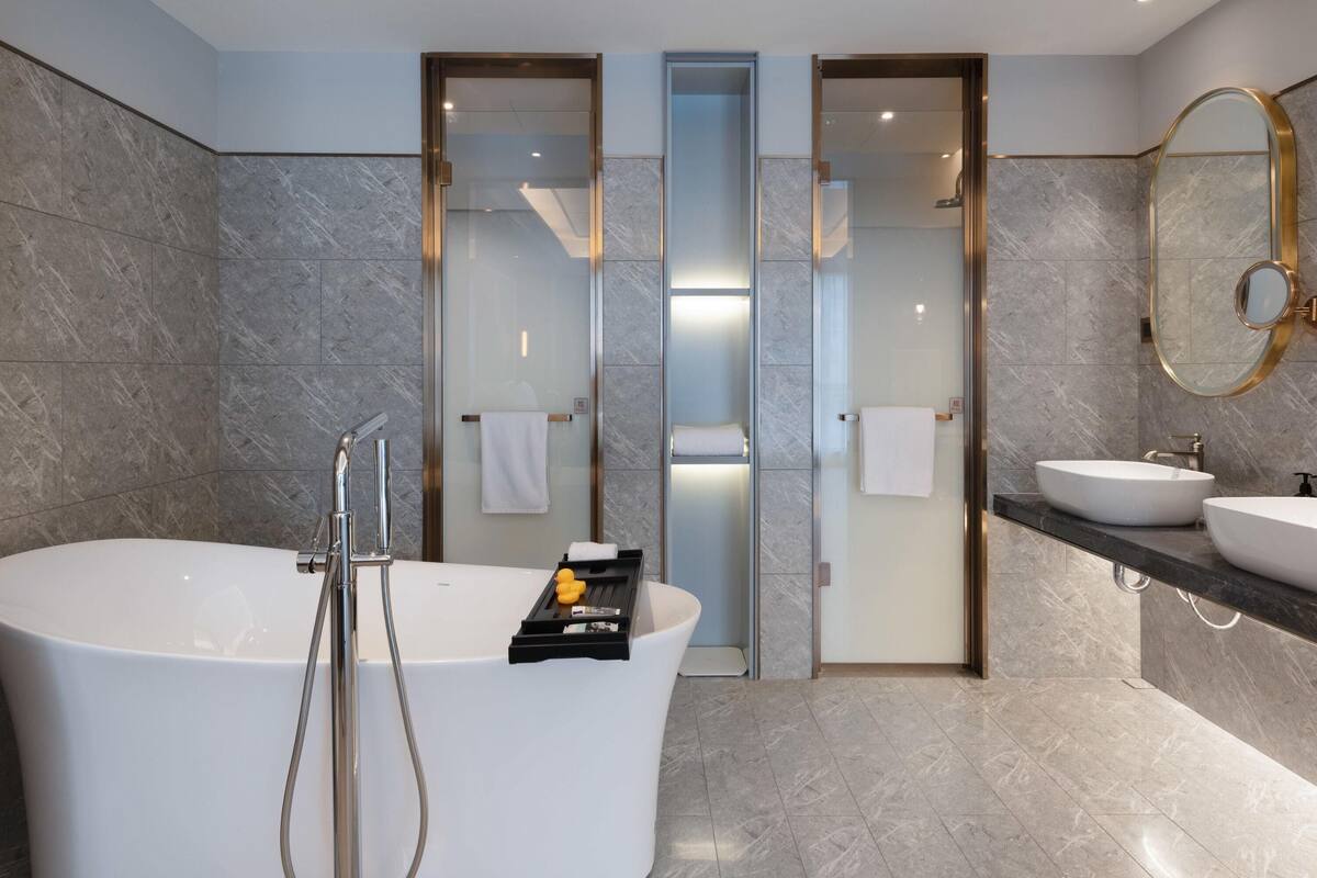 A modern bathroom with a freestanding bathtub, two sinks, and a glass-enclosed shower area.