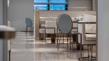 Eine moderne Hotellobby mit einer Sitzecke, einem Empfangsbereich und Blick auf die Stadt durch große Fenster.