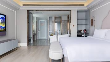 Ein modernes Hotelzimmer mit einem großen Bett, einem Fernseher, einem Schreibtisch und einem durchgegangene Tür einsehbaren Badezimmer.