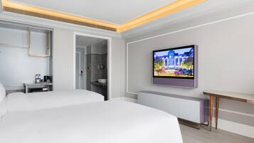 A modern hotel room with a large bed, a TV mounted on the wall, a bedside table with a lamp, and a bathroom visible through an open door.