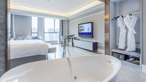 A modern hotel room with a large bathtub, a bed, a TV, and a robe rack. - Mercure Xian North (Xi'an)