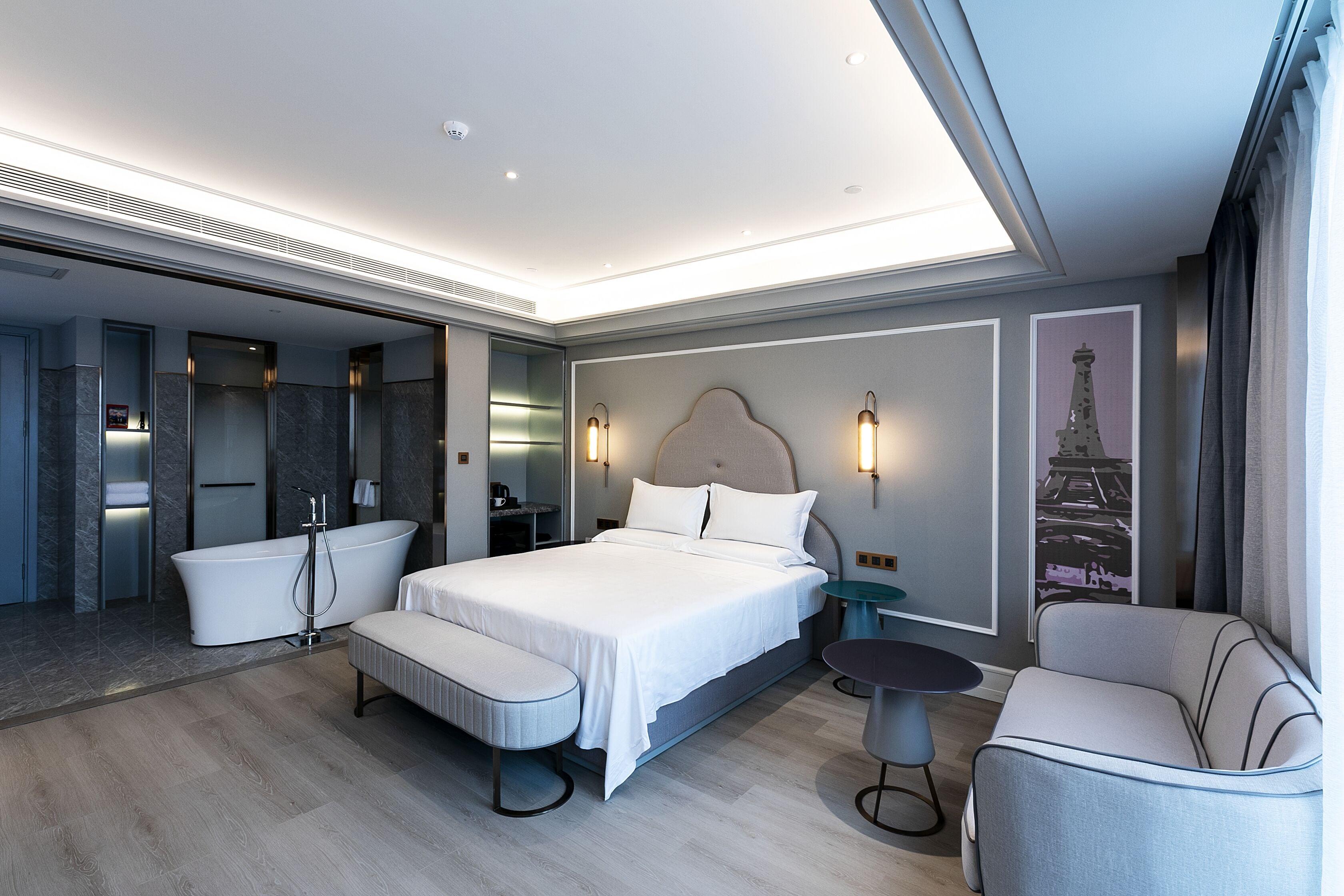 A modern hotel room with a large bed, a sitting area, a bathtub, and a small table.