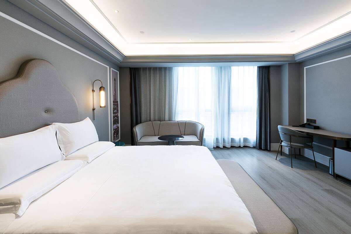 A modern hotel room with a large bed, a desk, a chair, and a sofa.