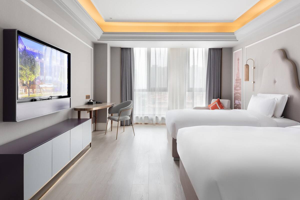 A hotel room with a bed, a desk, a TV, and a view of the city.
