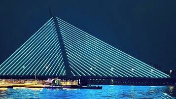 A large, illuminated bridge structure with a triangular design, spanning over a body of water.