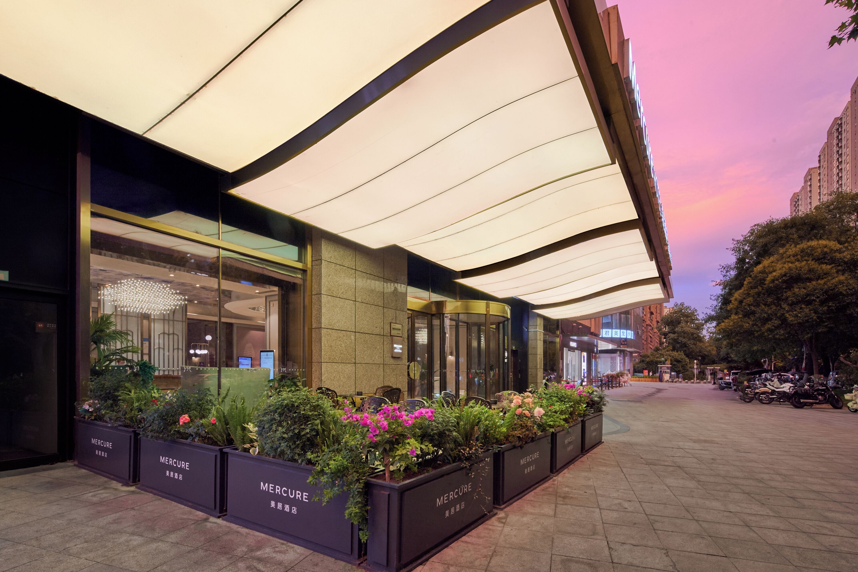 A hotel entrance with a covered walkway, glass doors, and planter boxes with greenery.