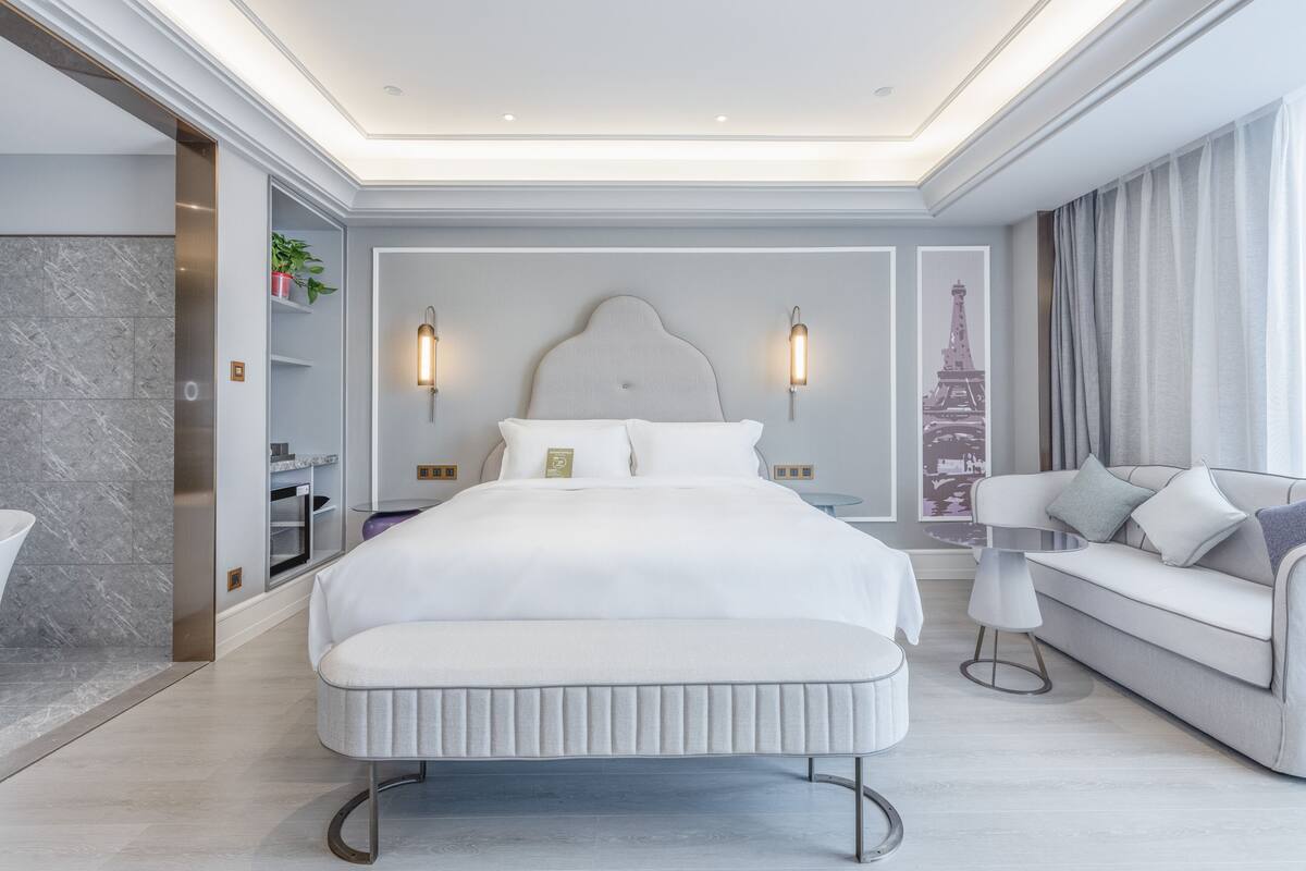 A modern hotel room with a large bed, a sofa, a small table, and a view of the Eiffel Tower.