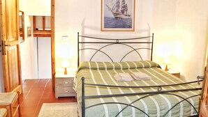 A bedroom with a bed, two bedside tables with lamps, a wooden wardrobe, and a framed picture on the wall. - Porto Rotondo Garden Flats (Olbia)
