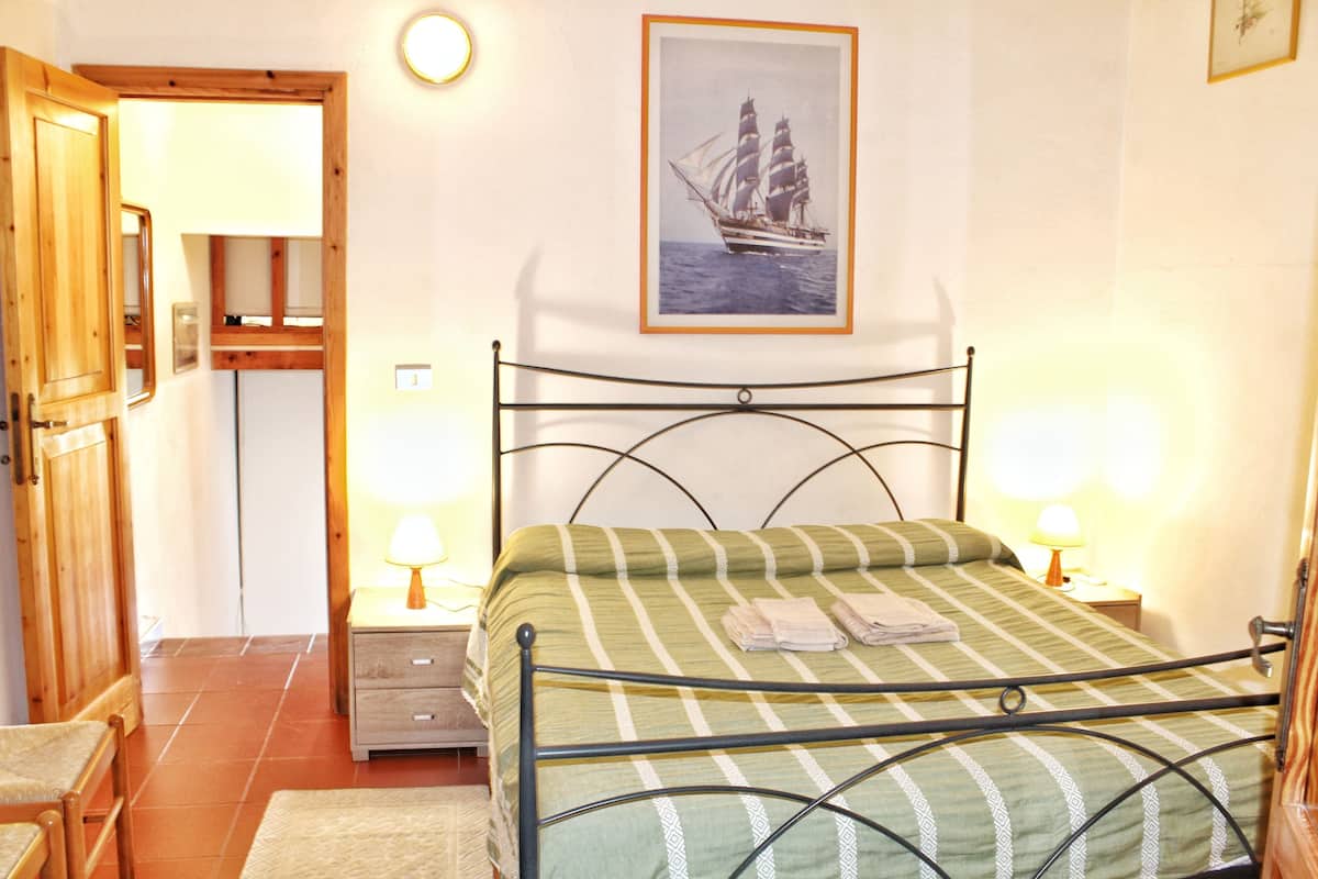 Ein Schlafzimmer mit einem Bett, zwei Nachttischen mit Lampen, einem Holzschrank und einem gerahmten Bild an der Wand.