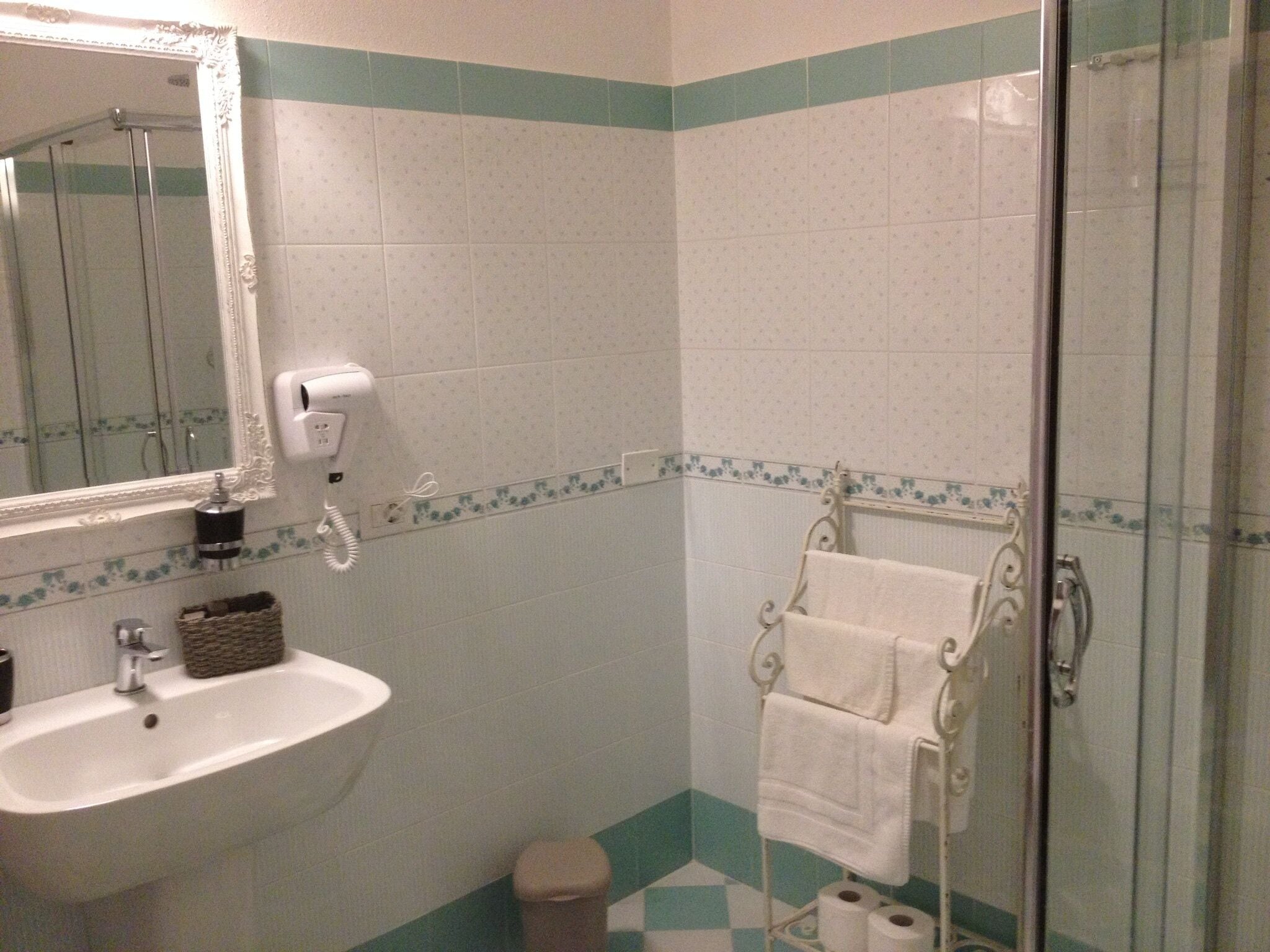 Une salle de bain équipée d’un lavabo, d’un miroir, d’un porte-serviettes et d’une cabine de douche en verre.
