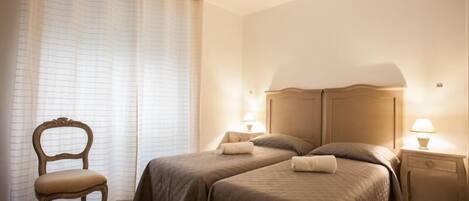 A hotel room with two beds, a chair, and a nightstand with lamps.