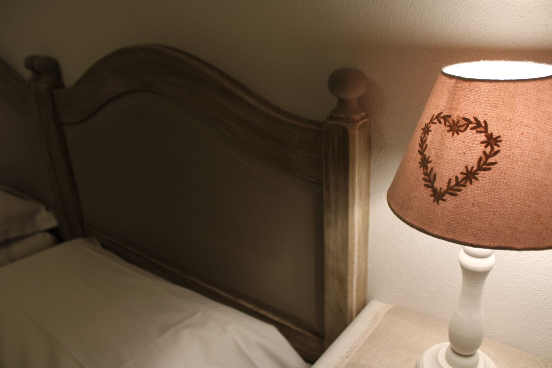 A bed with a wooden headboard and a nightstand with a lamp that has a heart-shaped design on the lampshade.