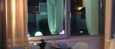 Un comedor con una mesa dispuesta para dos, una ventana con cortinas y vistas al exterior.