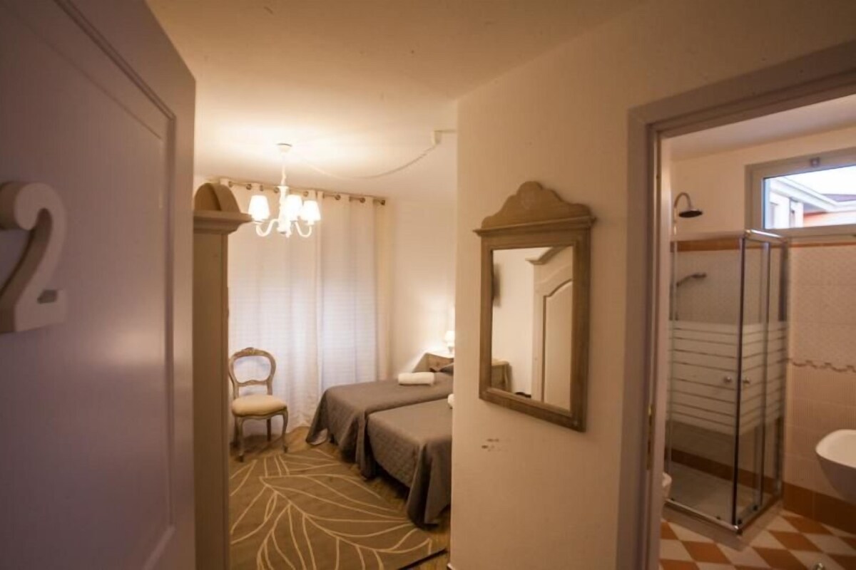 Habitación de hotel con cama, una silla, un espejo y zona de ducha.