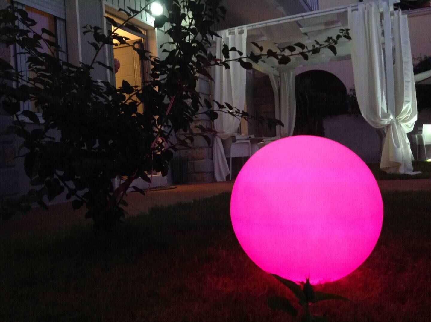 Una esfera rosa brillante en un jardín con un edificio al fondo.