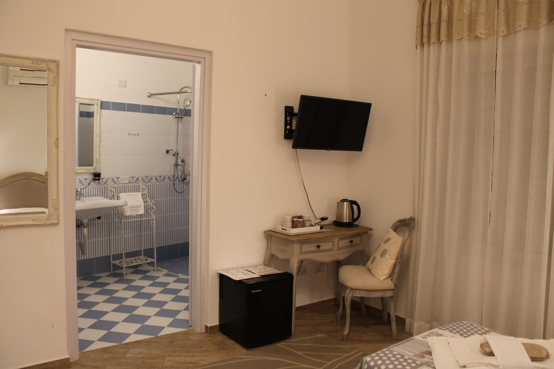 Hotelkamer met een geruit vloerkleed, een wastafel, een spiegel, een douche, een televisie, een klein kastje en een stoel.