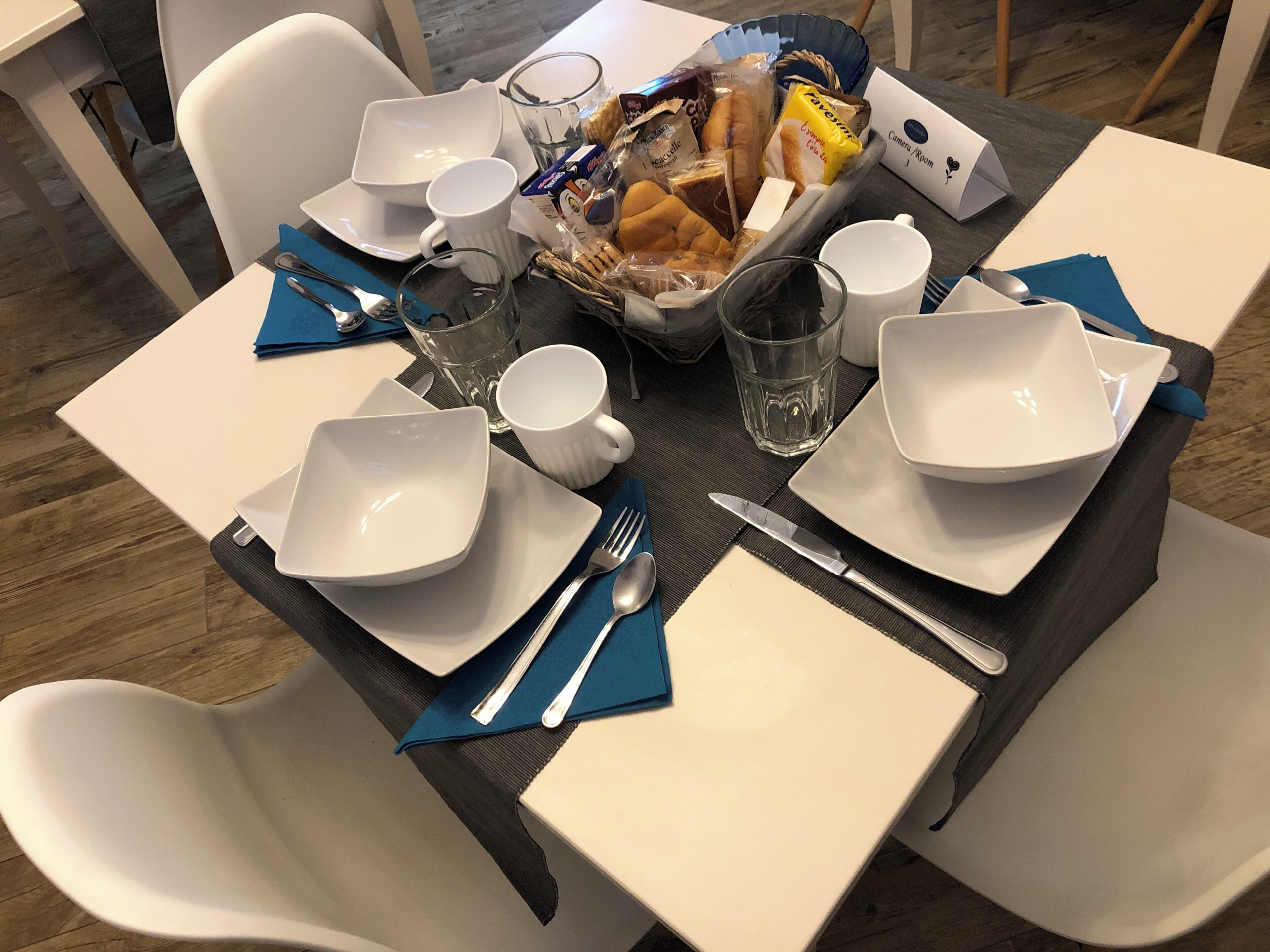 Une table à manger dressée avec des assiettes, des bols, des couverts et un panier de pain.