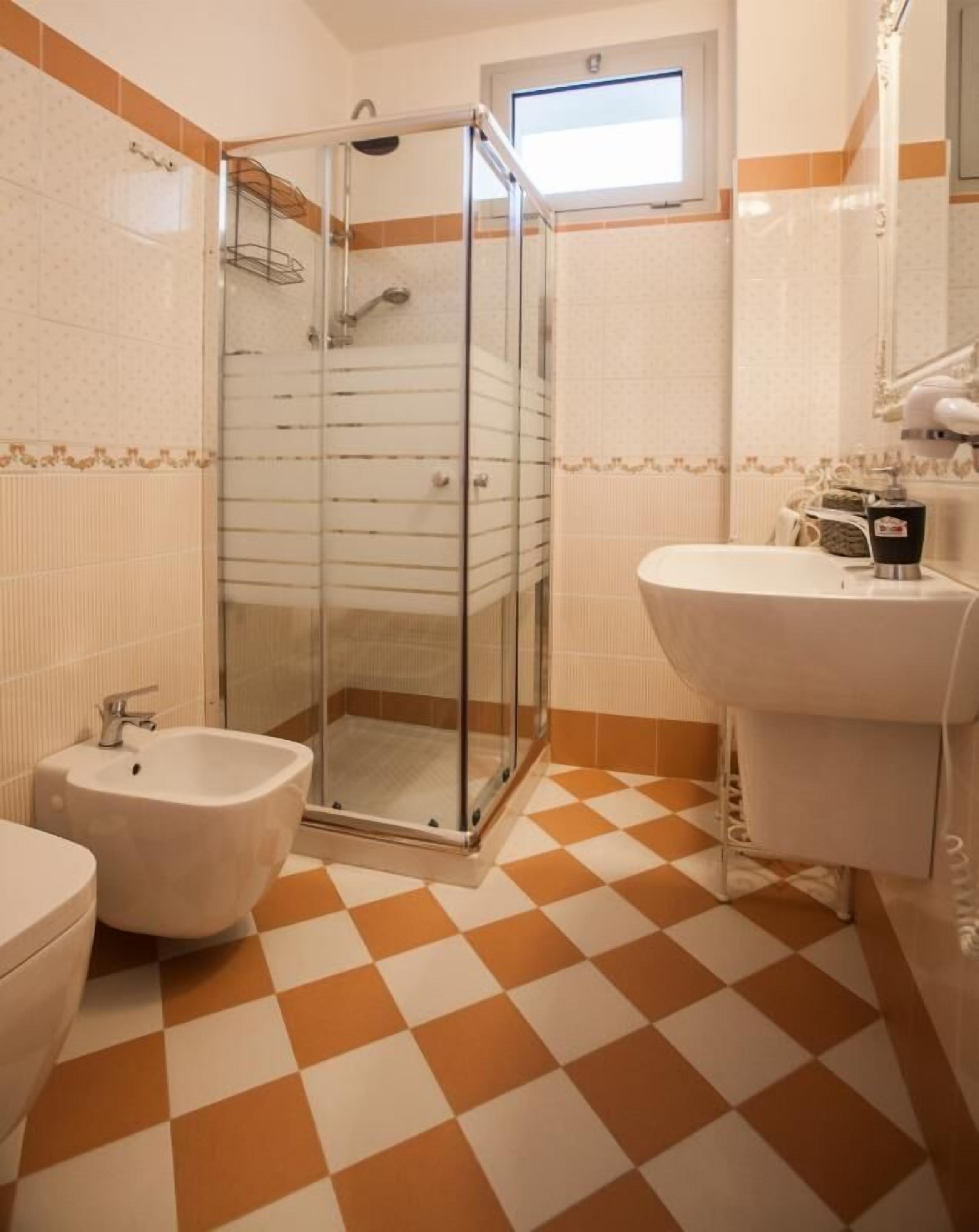 Ein Badezimmer mit einer Duschkabine, einem Bidet, einem Waschbecken und einem Schachbrettboden.