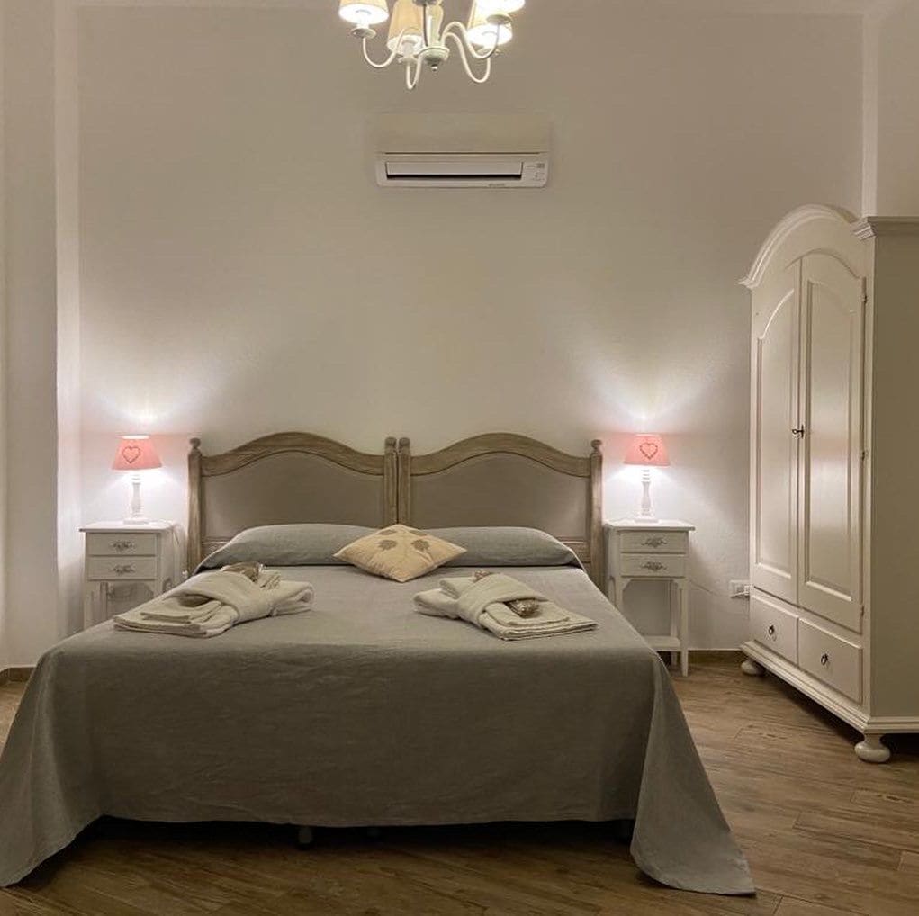 Un lit bien fait, avec une tête de lit, deux tables de chevet avec des lampes, une armoire et un appareil de climatisation fixé au mur.