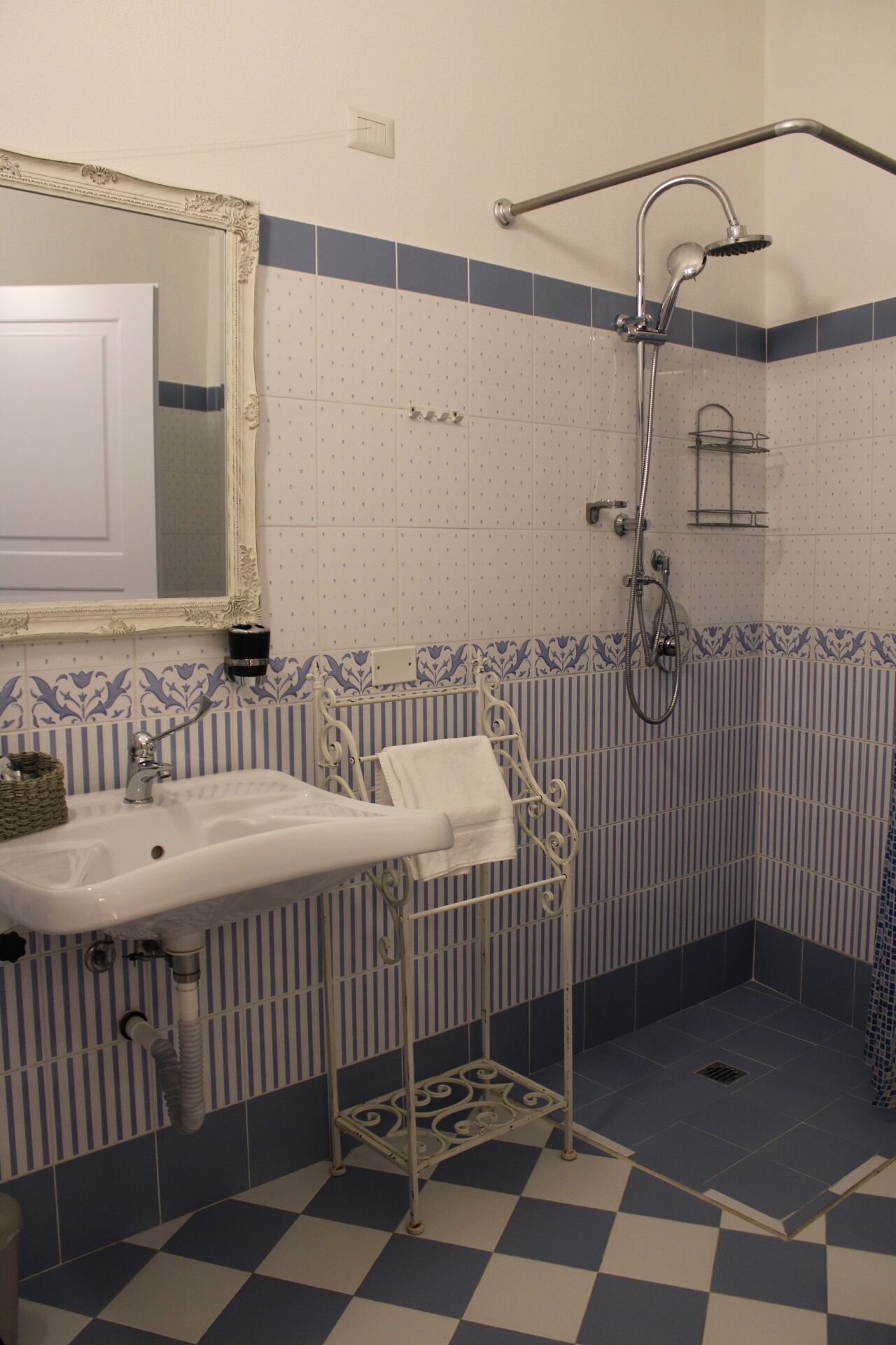 A bathroom with a white sink, a mirror, a shower with a grab bar, and blue and white patterned tiles.