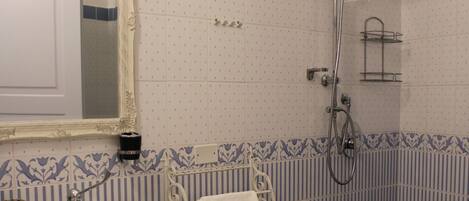 A bathroom with a white sink, a mirror, a shower with a grab bar, and blue and white patterned tiles.