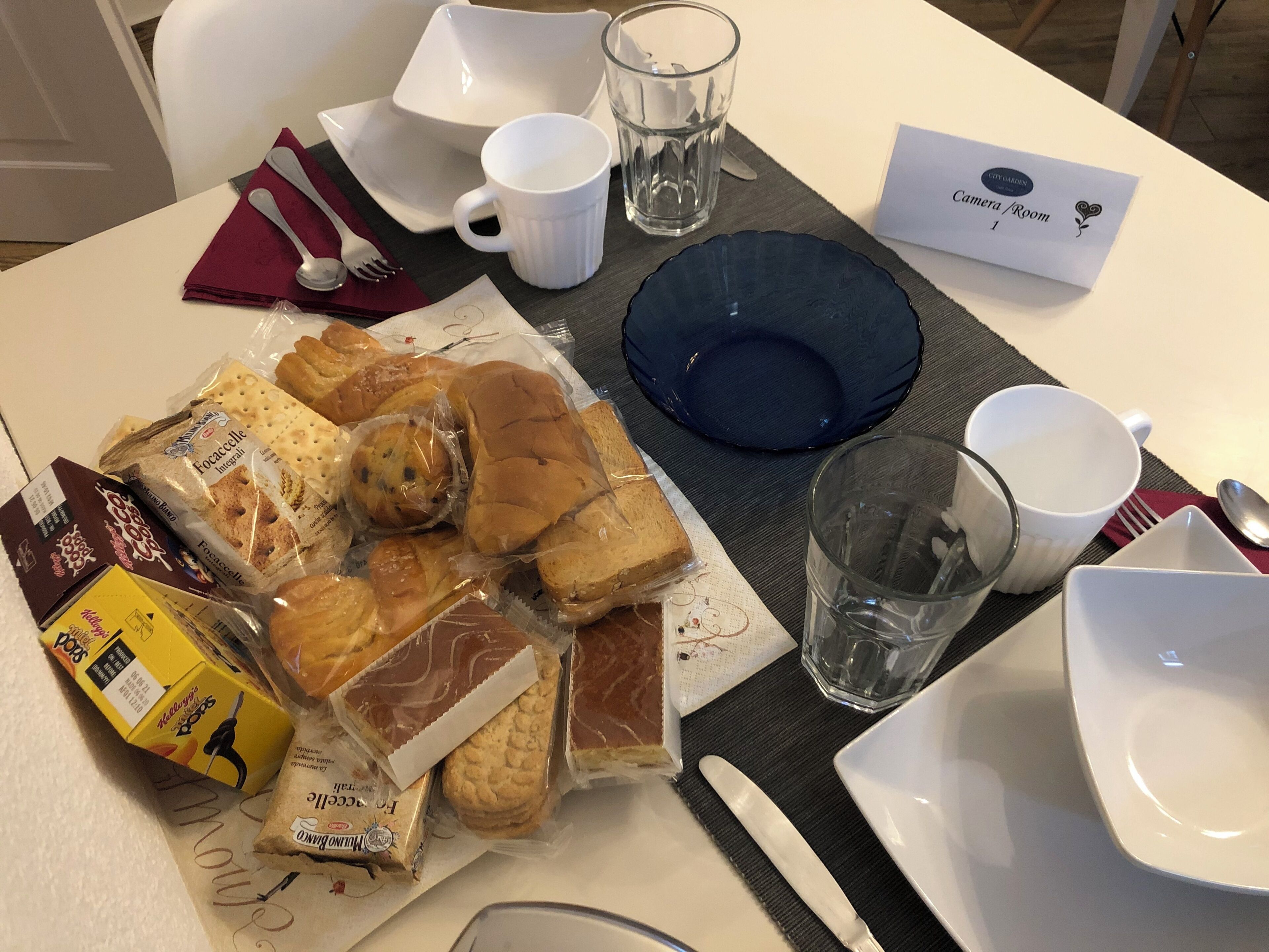 Une table de petit-déjeuner avec divers en-cas emballés, un couteau, une fourchette, un verre et une serviette.