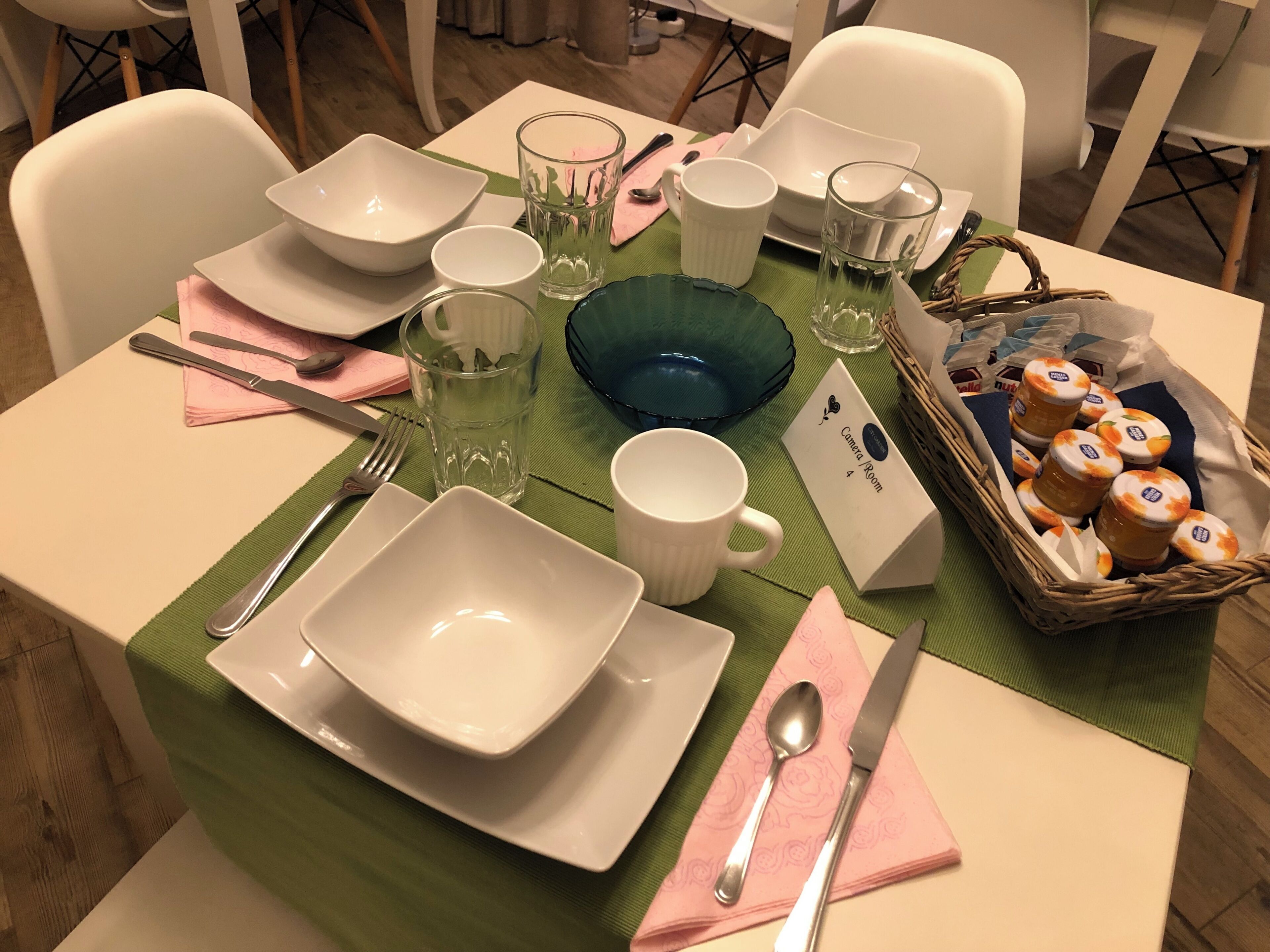 Una mesa de comedor dispuesta con platos, tazones, vasos y una cesta de alimentos.