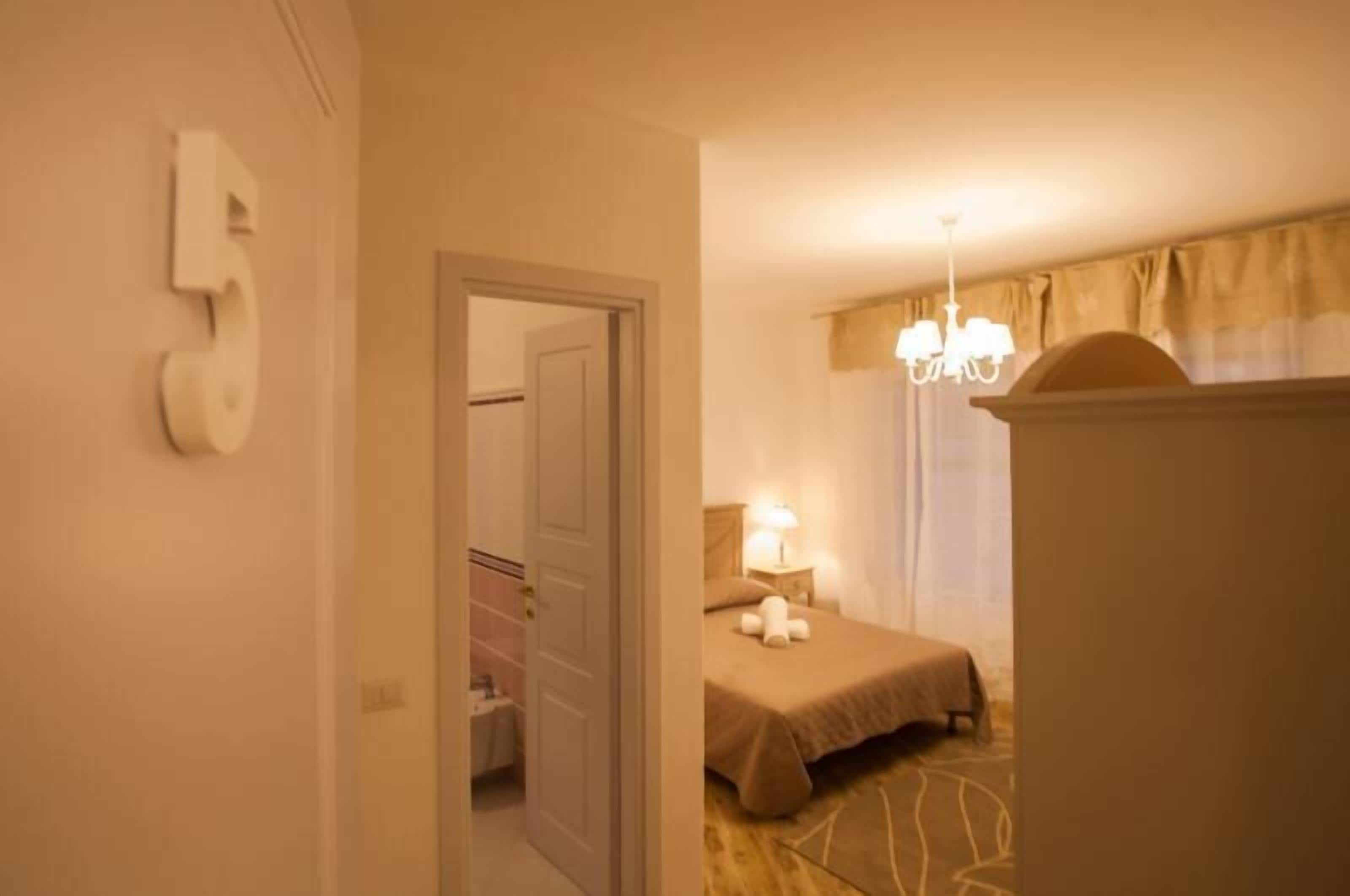 Habitació d'hotel amb un llit, una tauleta de nit, una làmpada, una pèndol i una porta amb el símbol de número.