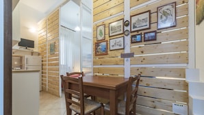 A dining area with a wooden table and chairs, a kitchen with a refrigerator and a TV, and a wall decorated with framed pictures. - Vittorio Emmanuele & Colosseo Studio (Rome)