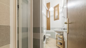 A bathroom with a glass shower enclosure, a washing machine, a toilet, and a sink with a wooden shelf. - Vittorio Emmanuele & Colosseo Studio (Rome)