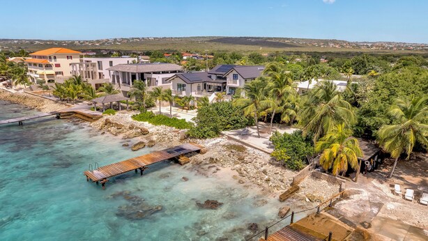 Una zona residencial costera con casas, un muelle de madera y aguas turquesas cristalinas.