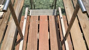 Una terraza de madera con barandas de metal que da a aguas claras y poco profundas.